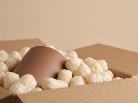 Ceramic mug packed with biodegradable cornstarch packing peanuts in a cardboard box for sustainable shipping and delivery