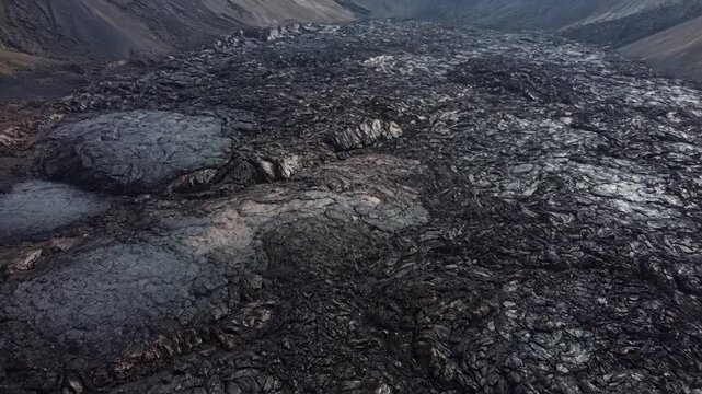 Aerial view of volcanic lava field. Cinematic drone footage of dark solidified magma rock formations.