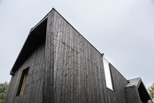 Low-angle view of a modern house clad in black Shou Sugi Ban timber, with angular rooflines, reflective glazing, textured boards, and overcast sky copy space