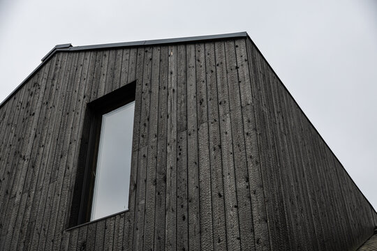 Low-angle view of a modern building clad in black Shou Sugi Ban timber, featuring vertical charred boards, a reflective window, geometric lines, and sky copy space