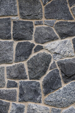 Close-up of an irregular gray natural stone wall with beige mortar joints, varied shapes, and a rough textured surface forming a full-frame architectural background