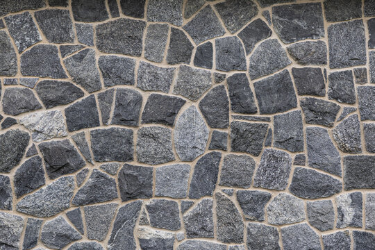 Close-up of an irregular gray natural stone wall with beige mortar joints, varied shapes, and a rough textured surface forming a full-frame architectural background