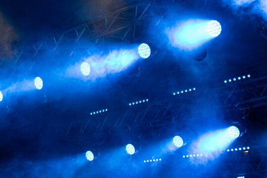 Bright blue LED stage spotlights project powerful beams through theatrical fog on a concert lighting rig, creating a dramatic live event atmosphere with copy space