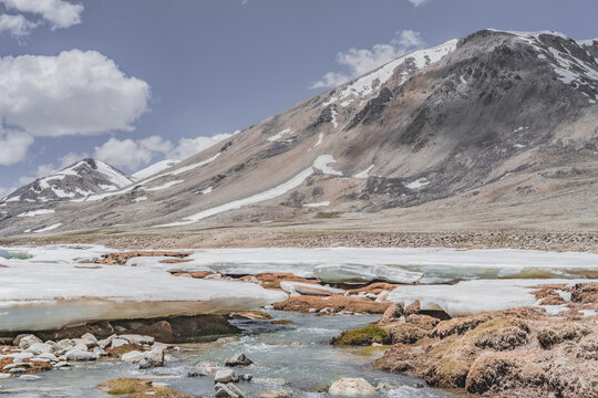 Landscape in the high Pamirs with rocky peaks and a river in a valley with melting snow. Panorama of rocky mountains on a sunny day and glaciers in a river valley