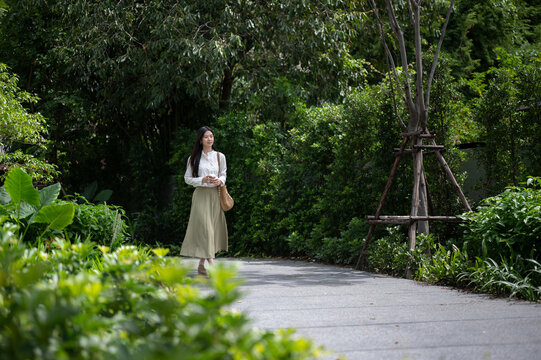 Young Asian woman holding coffee cup and enjoying a peaceful walk through tropical green garden park