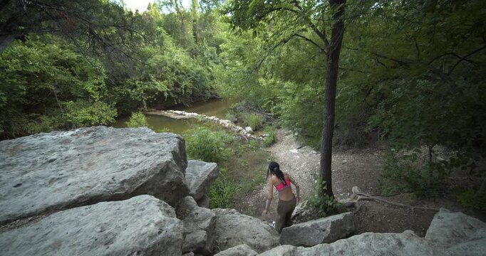 An authentic scene of a woman wellness hiking through a dense green forest trail in Kansas, approaching a calm river. Great for sustainability and outdoor adventure content.