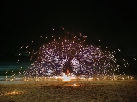 Fire dancer performing a spectacular fire spinning show on a tropical beach at night. Sparkling firework trail effect, perfect background for nightlife, beach party, travel, and entertainment concepts