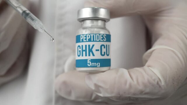 Gloved hands hold a GHK-CU peptide vial while a syringe moves in with a visible droplet, suggesting injection or clinical research use.
