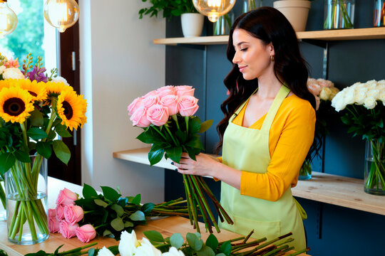 Young adult Caucasian woman arranging rose bouquet in flower shop, working as florist and preparing retail display. Ideal for small business, retail, handmade service marketing