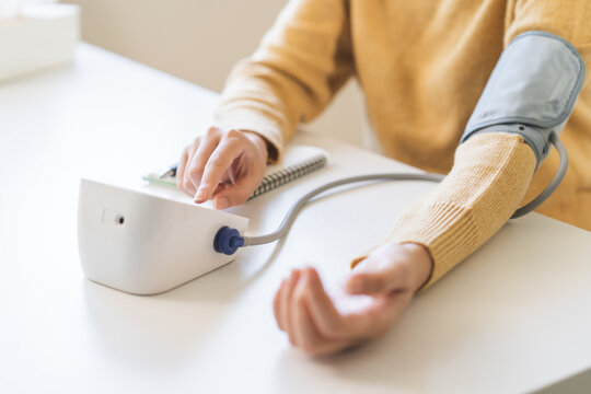 Close up of a person checking blood pressure with a digital monitor and cuff on arm at home table, healthcare lifestyle and hypertension medical examination concept.