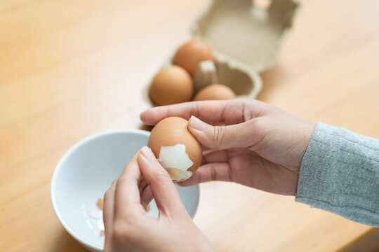 Protein in food, keto diet asian young woman hand peeling, shelling chicken boiled egg, prepares ingredient for breakfast meal on table at home. Removing egg shell, cleaning egg, health care concept.