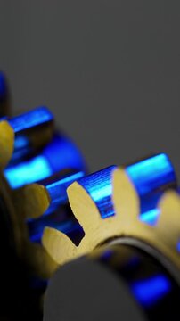Blue and Gold Gears in Motion. Macro view of interlocking metal cogwheels rotating under blue light.