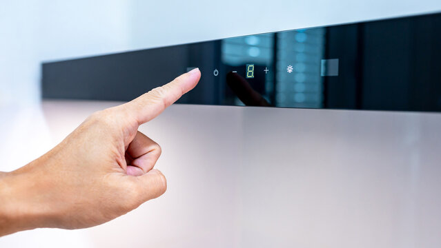 Hand touching digital switch panel on modern black kitchen hood to operate extractor fan and light. Adjusting mode of cooker hood. Home appliance in the kitchen