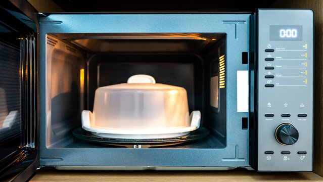Open door microwave oven with plastic plate cover inside. Digital timer display, mode buttons and knob on control panel. Home appliance in the kitchen