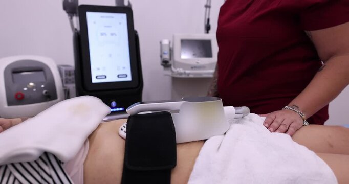 Patient undergoing a non invasive fat reduction procedure on her abdomen. With a professional aesthetician operating advanced body contouring and muscle stimulation equipment in a modern beauty salon