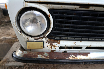 Fototapeta premium Close up of the rusty front end of an old vintage automobile with peeling paint, corrosion and weathered metal. Concept of aging vehicles, deterioration and restoration.