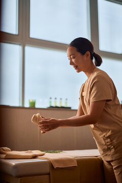 Smiling Korean spa therapist preparing massage room for treatment.