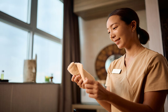 Smiling spa therapist preparing clean towels for massage therapy at wellness center.