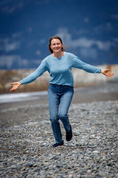 Woman smiles, running joyfully on pebble beach
