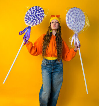 Full-body portrait of cheerful woman holding oversized lollipops against vibrant