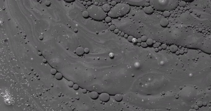 Abstract dark fluid texture. Macro view of viscous gray liquid with bubbles and organic swirls, slow gentle flow creating glossy reflections.
