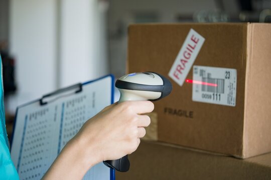 Person scanning a fragile cardboard parcel with handheld laser barcode reader cardboard logistics shipping