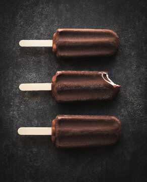 Top view of three chocolate covered ice cream bars on slate