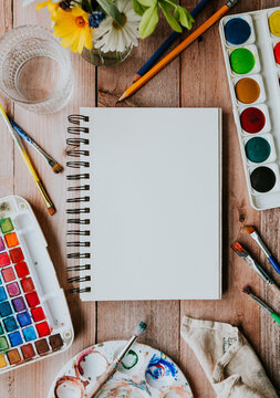 Artist workspace flat lay with blank sketchbook and watercolors