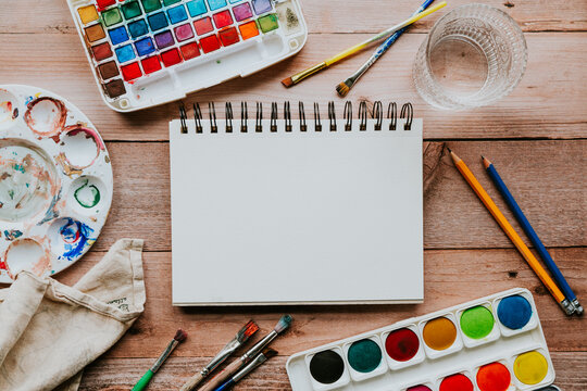 Blank sketchbook with watercolor painting supplies on wood table