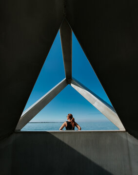 Woman looks out at calm water through a triangle