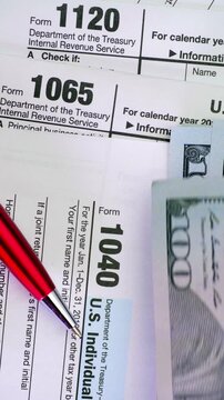 US Tax Forms with Cash Payment Concept. Close-up of IRS tax documents, one hundred dollar bills and red pen illustrating taxation, accounting and personal finance.