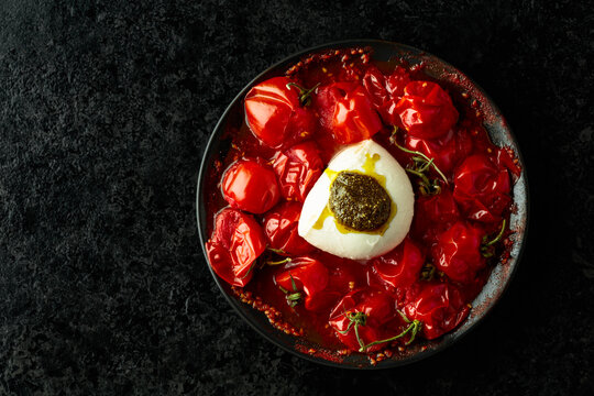 Mozzarella with pesto sauce and roasted red cherry tomatoes on a black background.