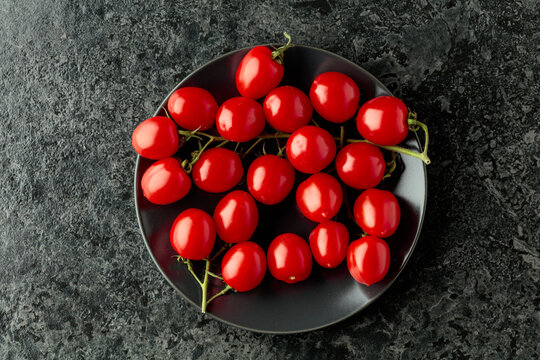 Small red cherry tomatoes on a black plate.