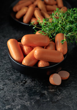 Boiled sausages with thyme on a black stone table.