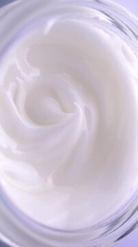 White Cream Swirling. Thick glossy cream moves in smooth folds, creating a soft abstract cosmetic texture.