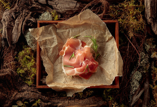 Prosciutto with rosemary on a paper in wooden box.