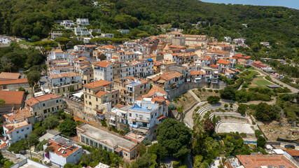 Fototapeta premium Panoramic aerial view of San Felice Circeo historic village nestled on a green hillside with traditional white buildings and orange rooftops under a bright sunny sky in Lazio, Italy.
