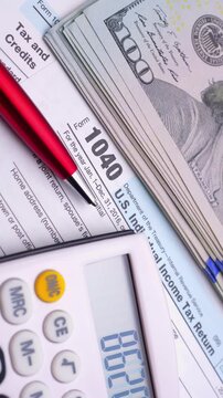 Close-up of US tax form, calculator, pen and one hundred dollar bills for finance and accounting concepts.