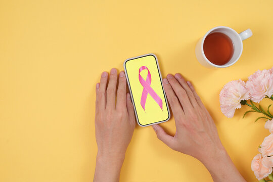Flat lay of hands near smartphone with pink ribbon for breast cancer awareness