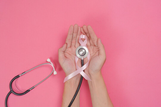 Open hands holding pink ribbon and stethoscope for breast cancer awareness and health checkup