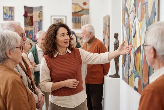 Museum guide explaining abstract painting to a group of elderly visitors in an art gallery