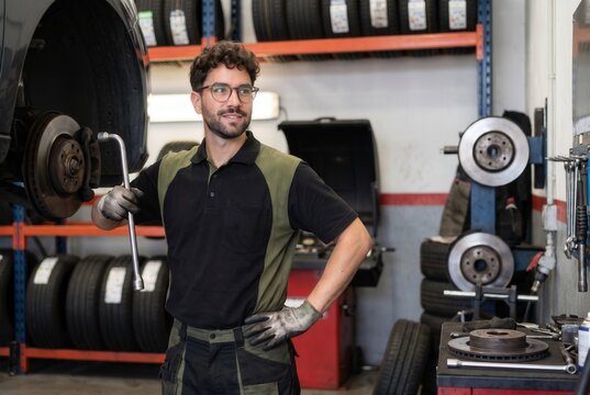 Auto mechanic standing in garage holding wrench with car components