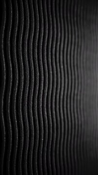 Black wavy ribbed texture slow pan. Close-up of deep black textured surface with vertical wavy ridges. Smooth linear camera movement reveals shifting light and shadow across the pattern.
