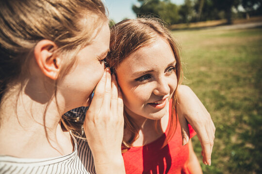 Two teenage girls whispering in park