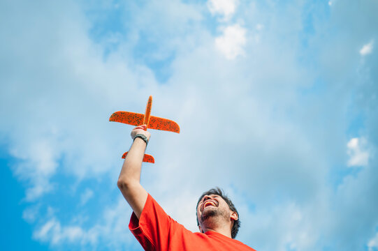 A happy man launches an orange toy airplane into the summer sky