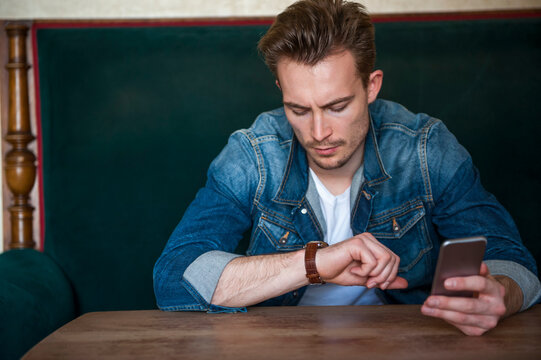 Portrait of angry young man sitting in a coffee shop checking the time
