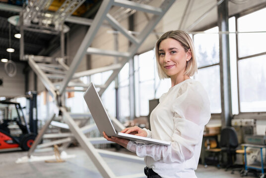 Portrait of smiling young woman using laptop in a factory
