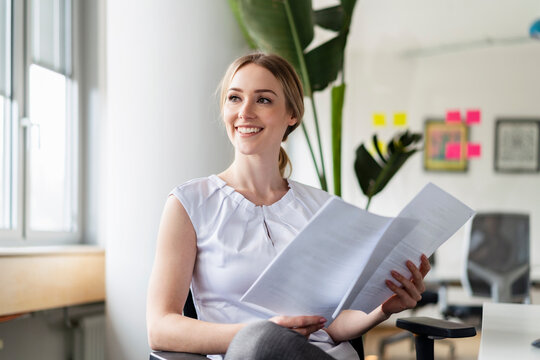 Contemplating businesswoman with documents smiling while looking away in office