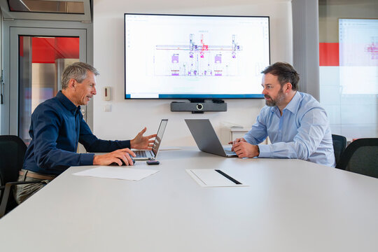 Businessmen discussing engineering plans on laptops in an office