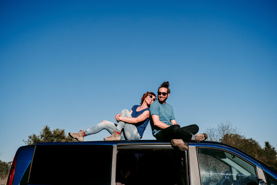 Happy couple sitting on the roof of a minivan